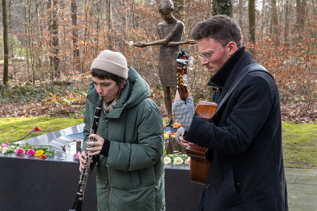 Eine Frau und ein Mann machen Musik vor der Skulptur „Trauerndes Mädchen am Tränenmeer“ auf dem Heidefriedhof